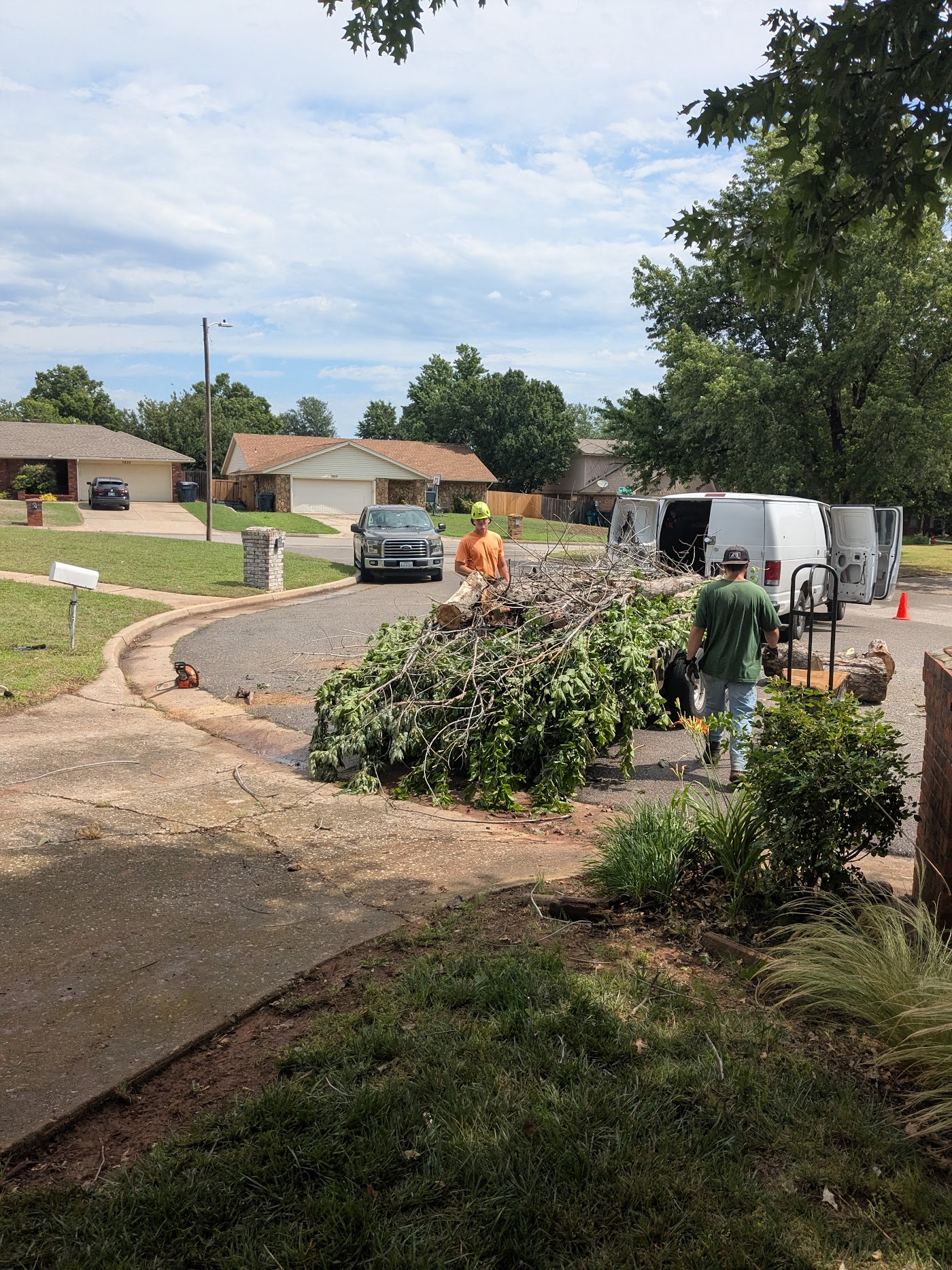 Prairie Wind crew clearing cut limbs from a Norman driveway beside the work van